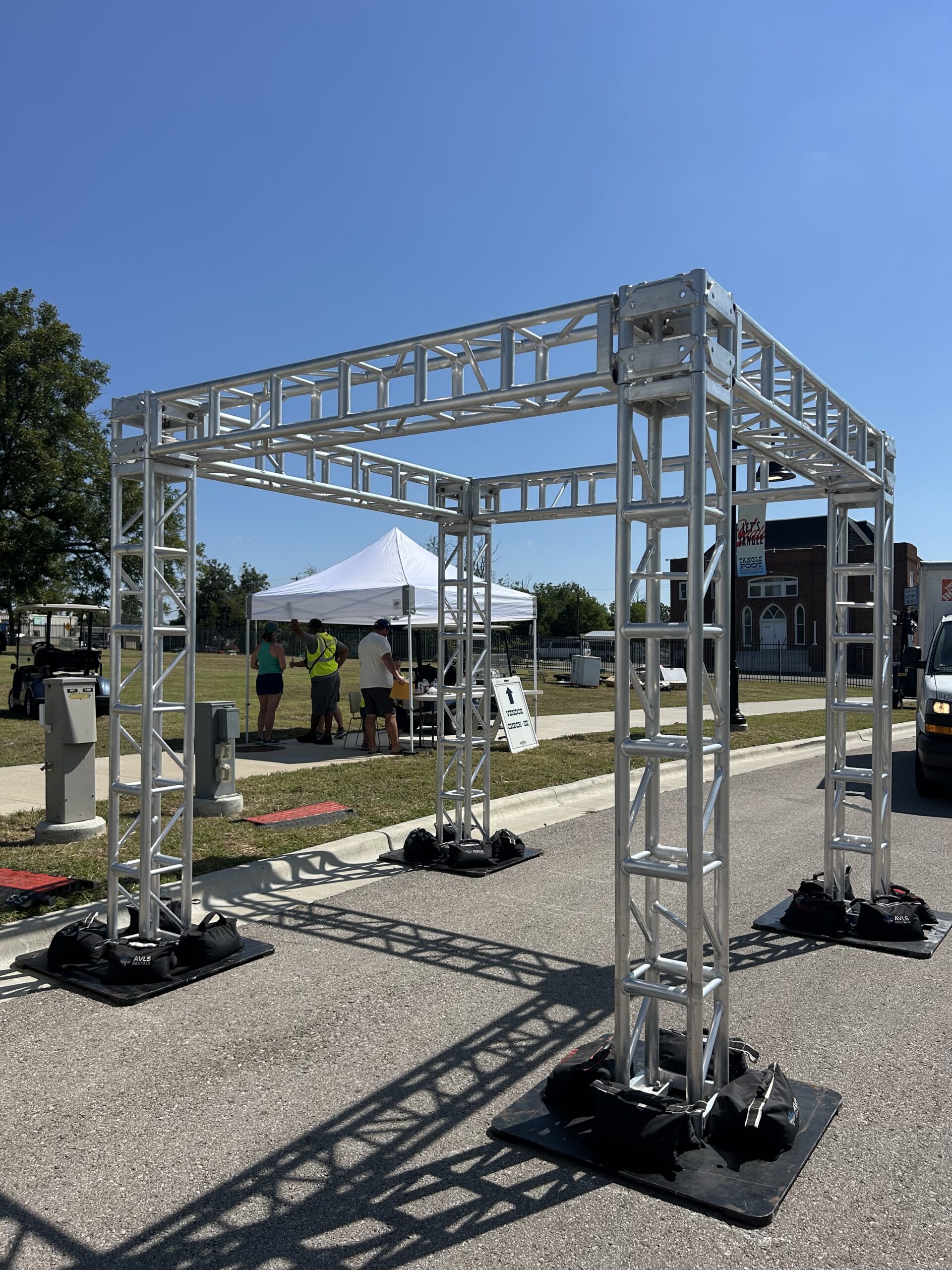 Outdoor truss structures: 12x12 box truss cube frame on steel base plates with sandbag ballast at an outdoor event